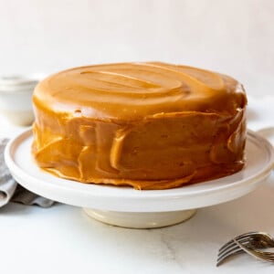 Caramel cake on a white cake stand.