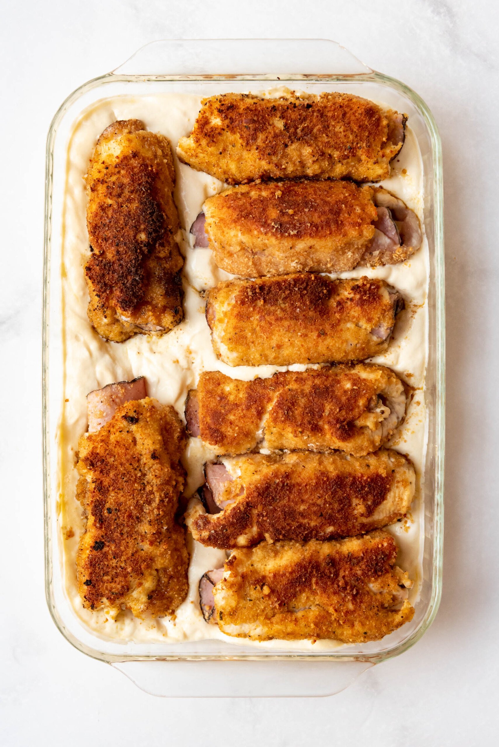 PIeces of browned chicken cordon bleu nestled in a creamy sauce ready to go into the oven.
