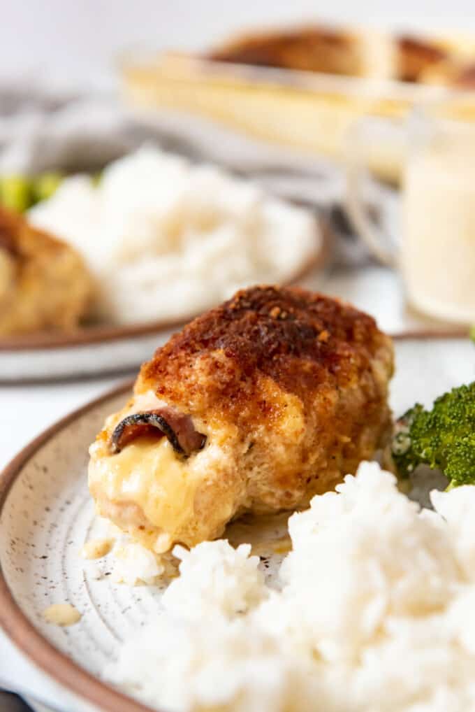 Chicken cordon bleu on a plate with rice and broccoli beside it and other dinners in the background.