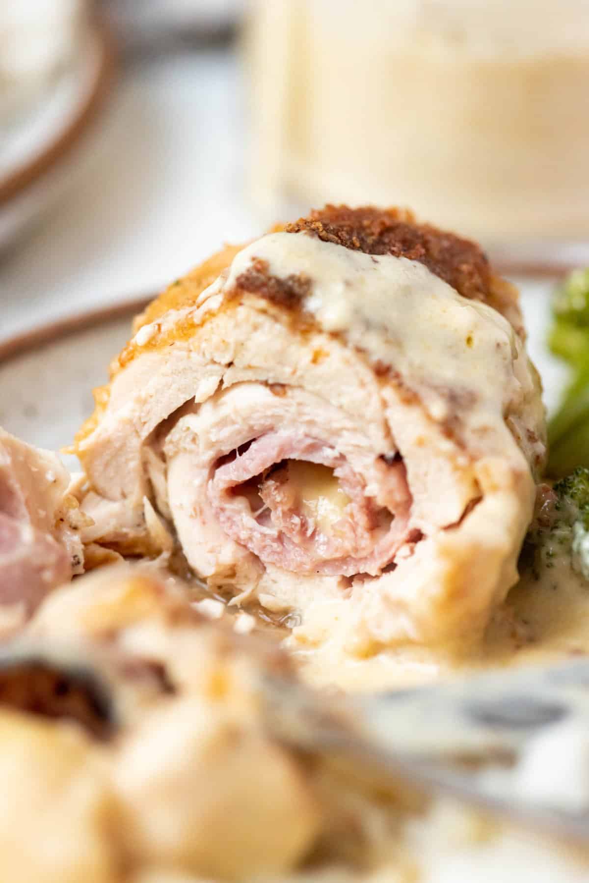 A piece of chicken cordon bleu that has been sliced in half to show the inside of ham and swiss cheese.