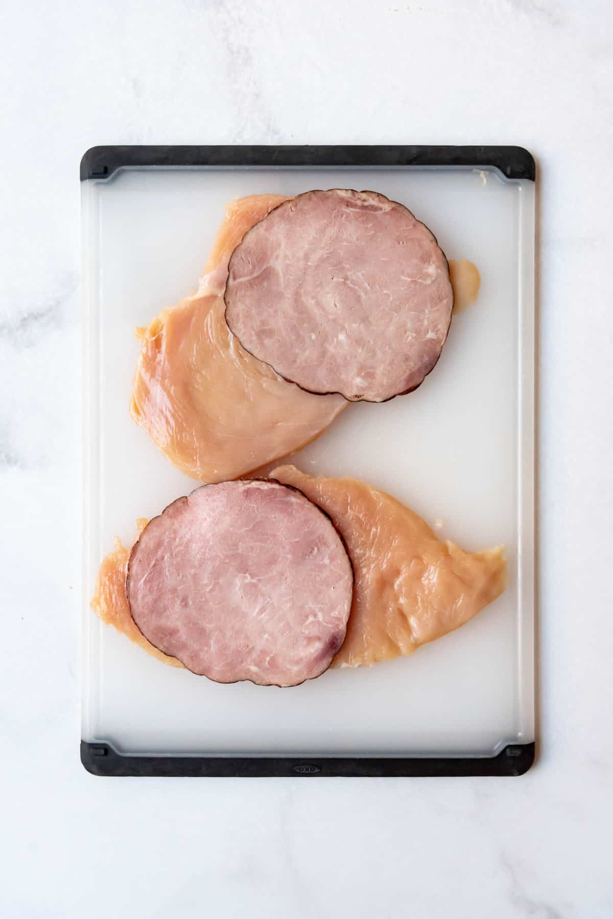 Slices of ham on top of two chicken breasts that have been pounded flat.