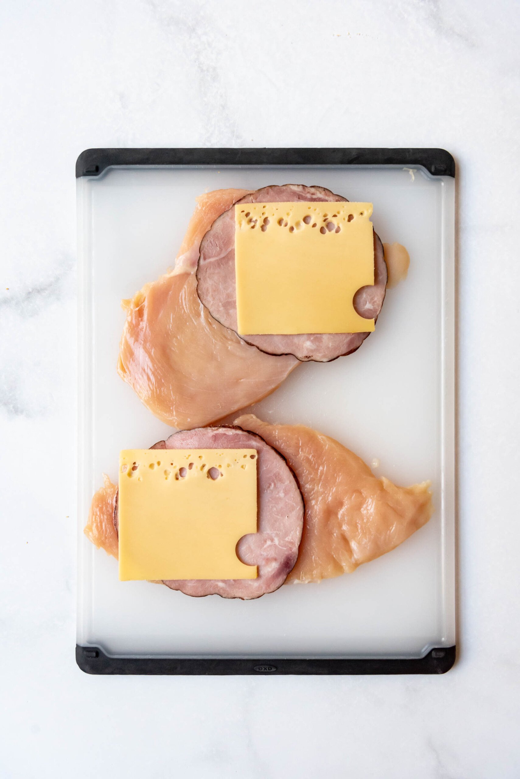 Adding a slice of swiss cheese on top of each piece of chicken breast and ham.