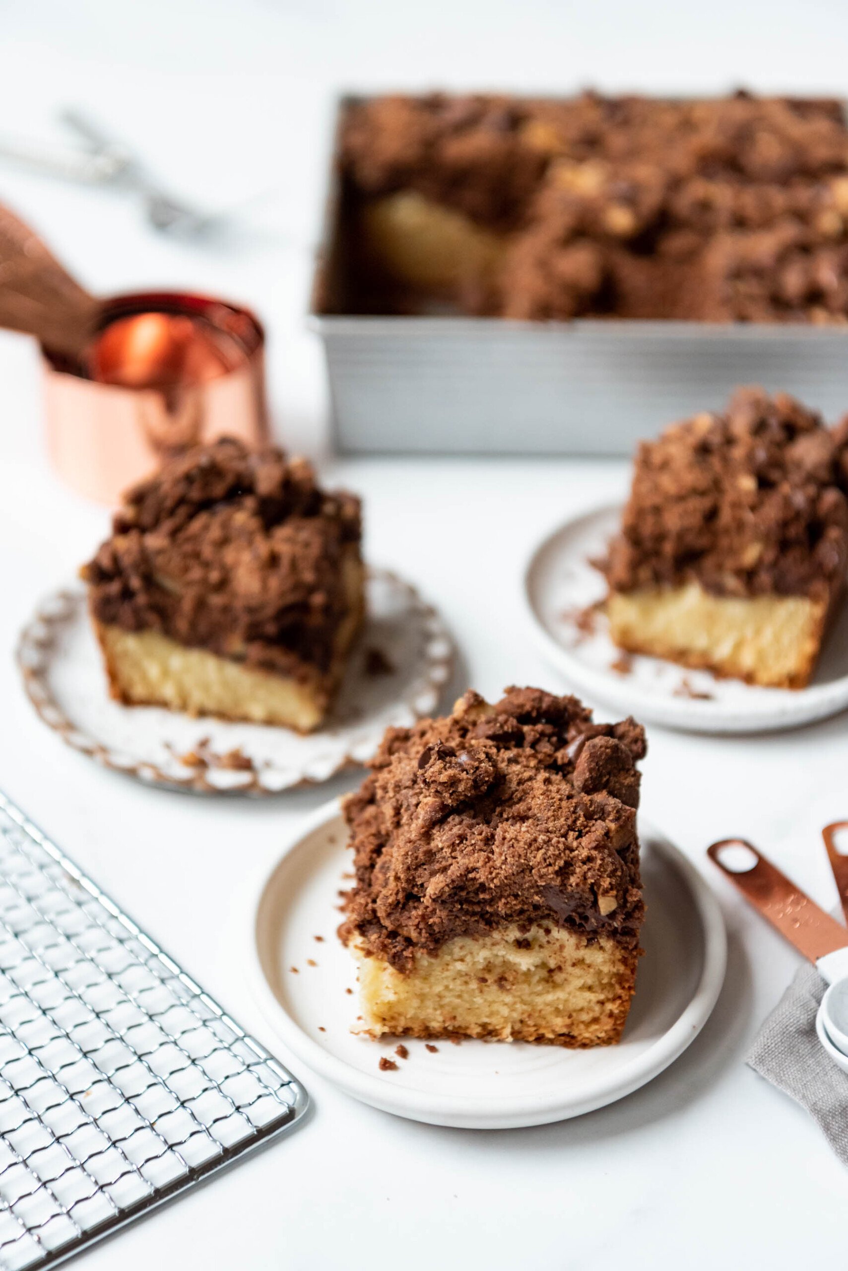 Slices of chocolate pecan crumb cake on small plates in front of a baking dish and measuring cups.