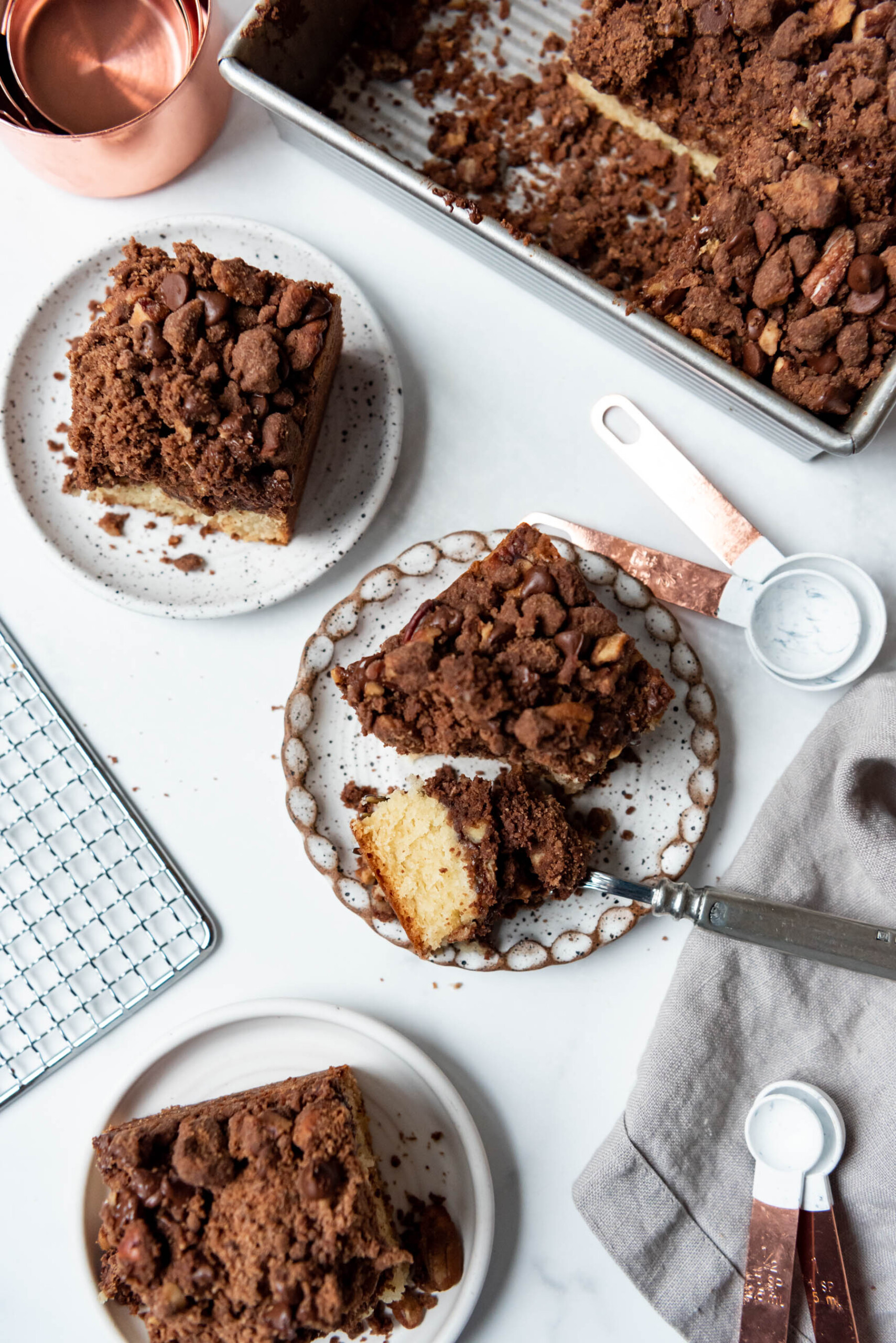 An overhead image of slices of chocolate pecan crumb cake on plates with a fork holding a bite of cake on one plate.