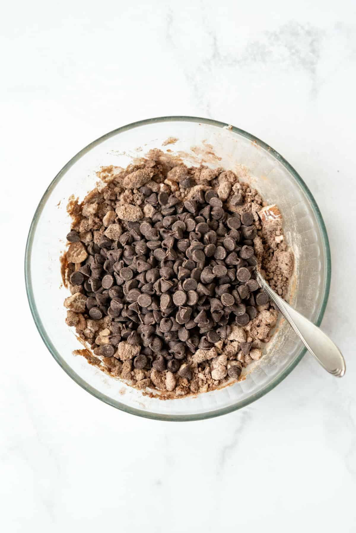 Adding chocolate chips to crumb topping in a bowl with a spoon.