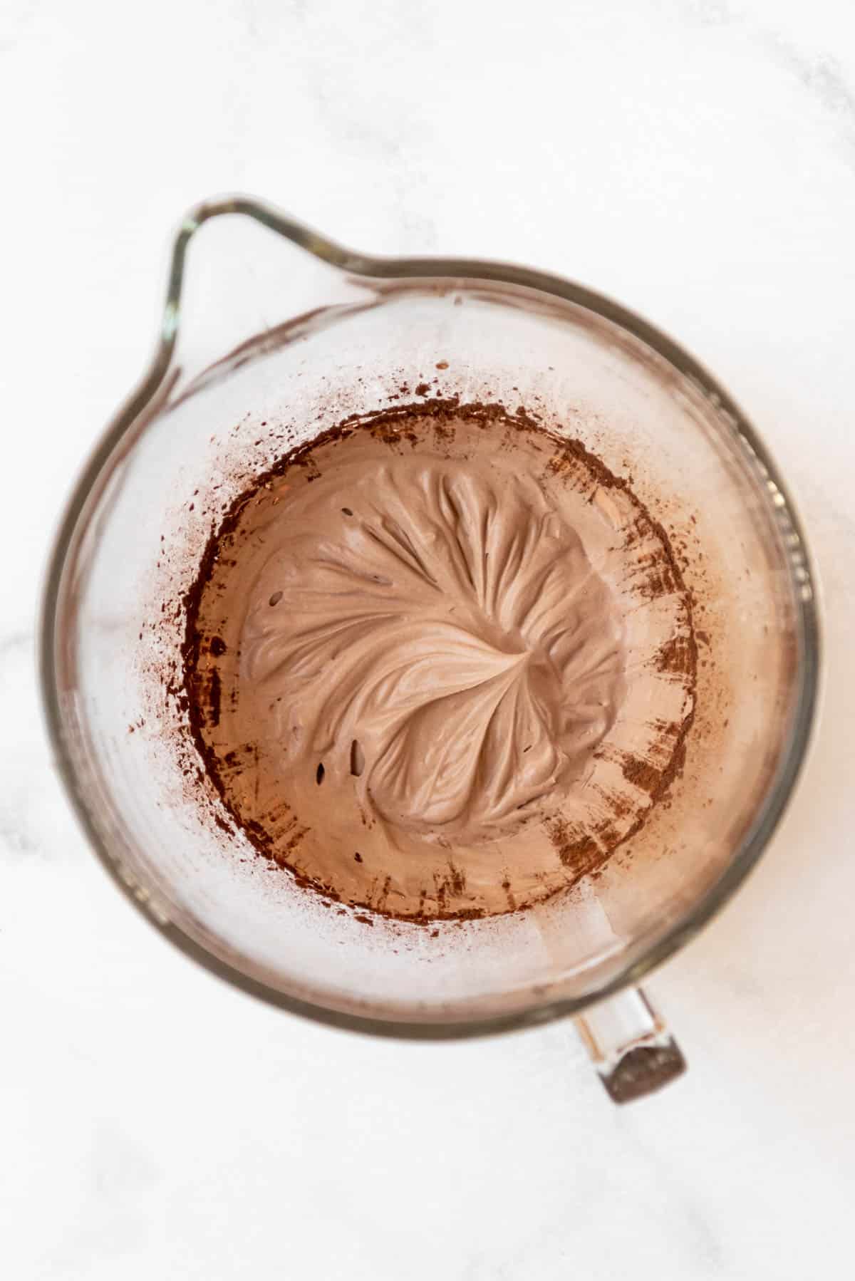 Chocolate whipped cream in a glass mixing bowl with cocoa powder around the edges that needs to be mixed in.