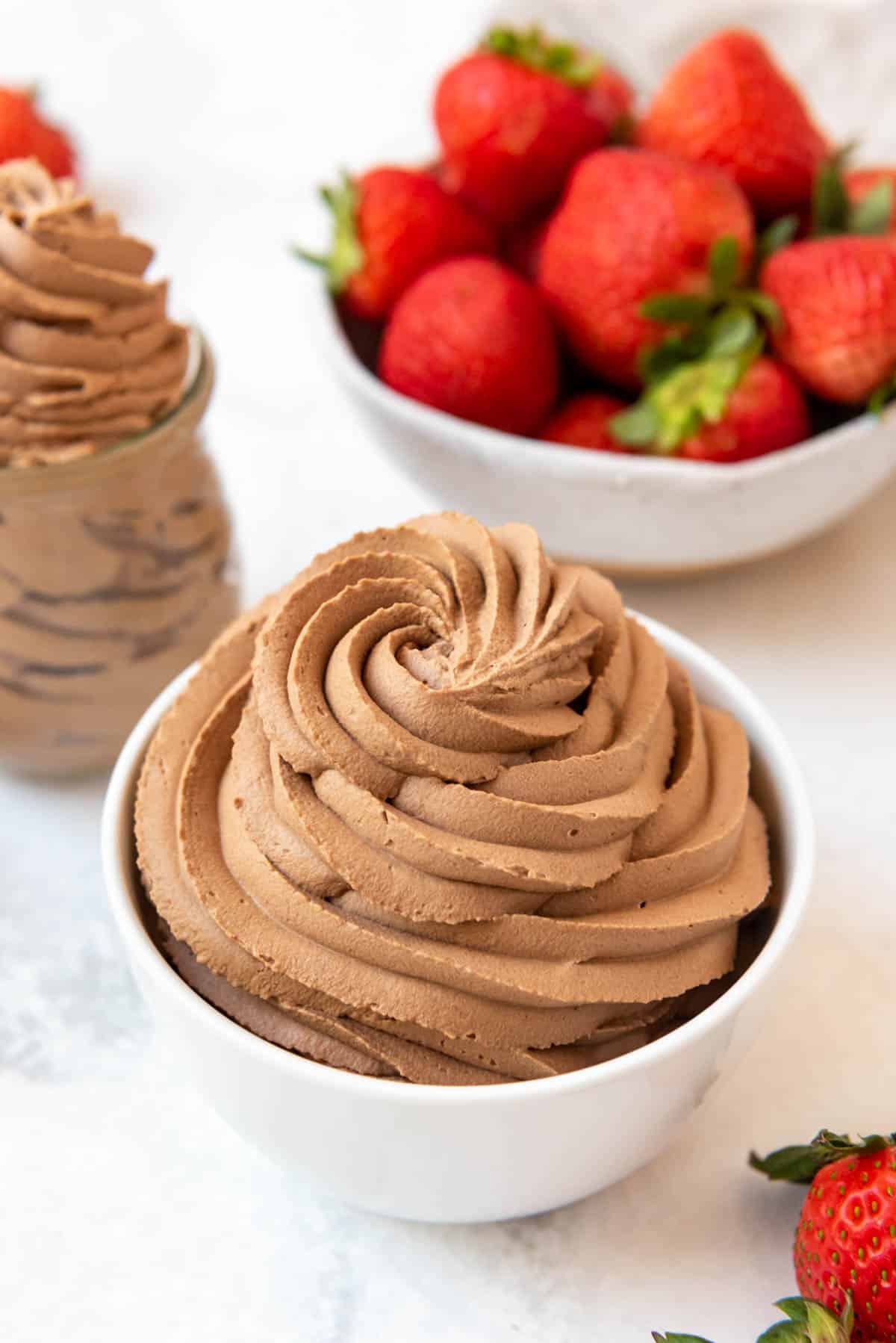 A bowl of chocolate whipped cream with a bowl of strawberries behind it.