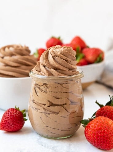 A glass jar filled with piped chocolate whipped cream surrounded by strawberries.