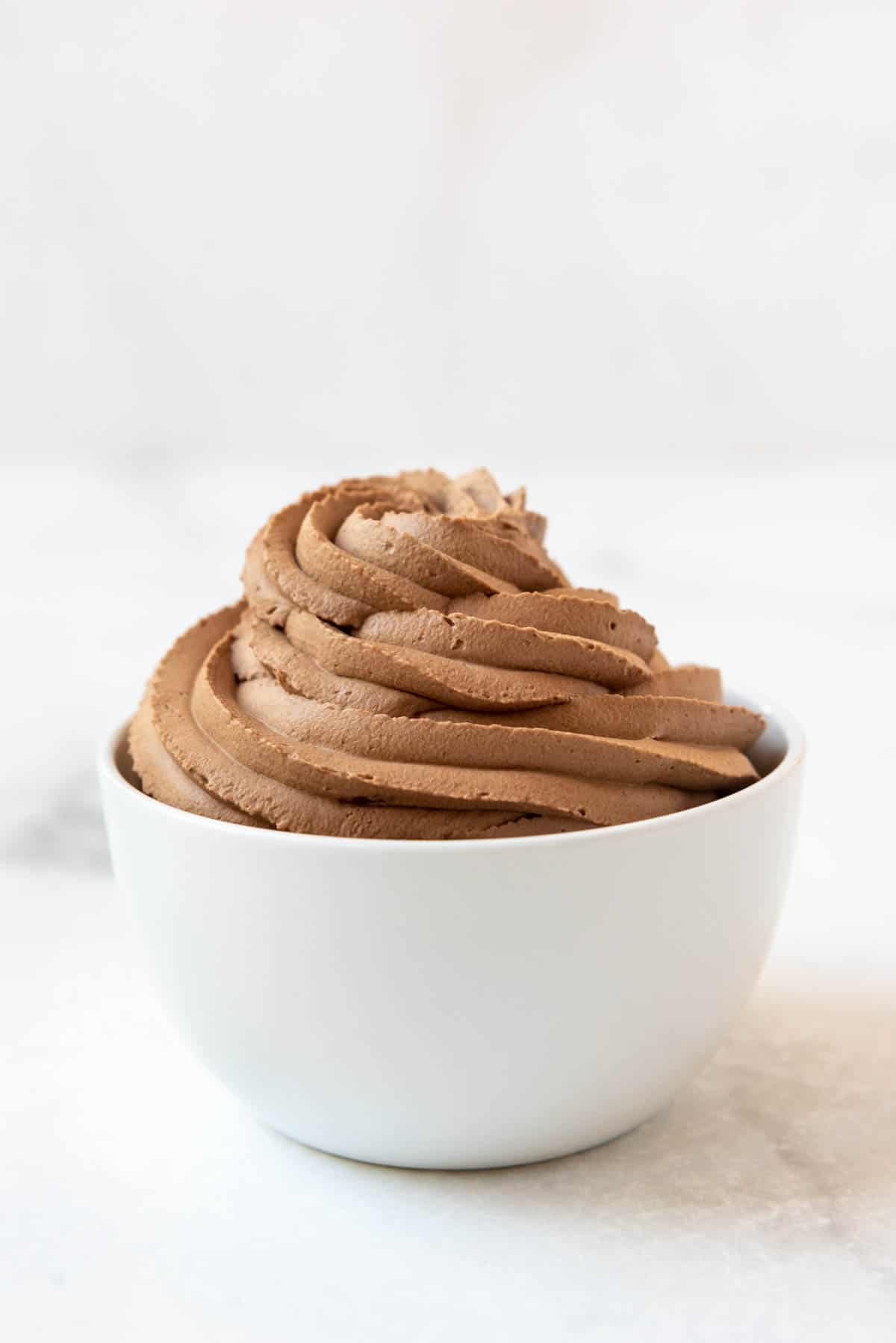 Close-up of a chocolate whipped cream swirl coming out of the top of a white bowl.