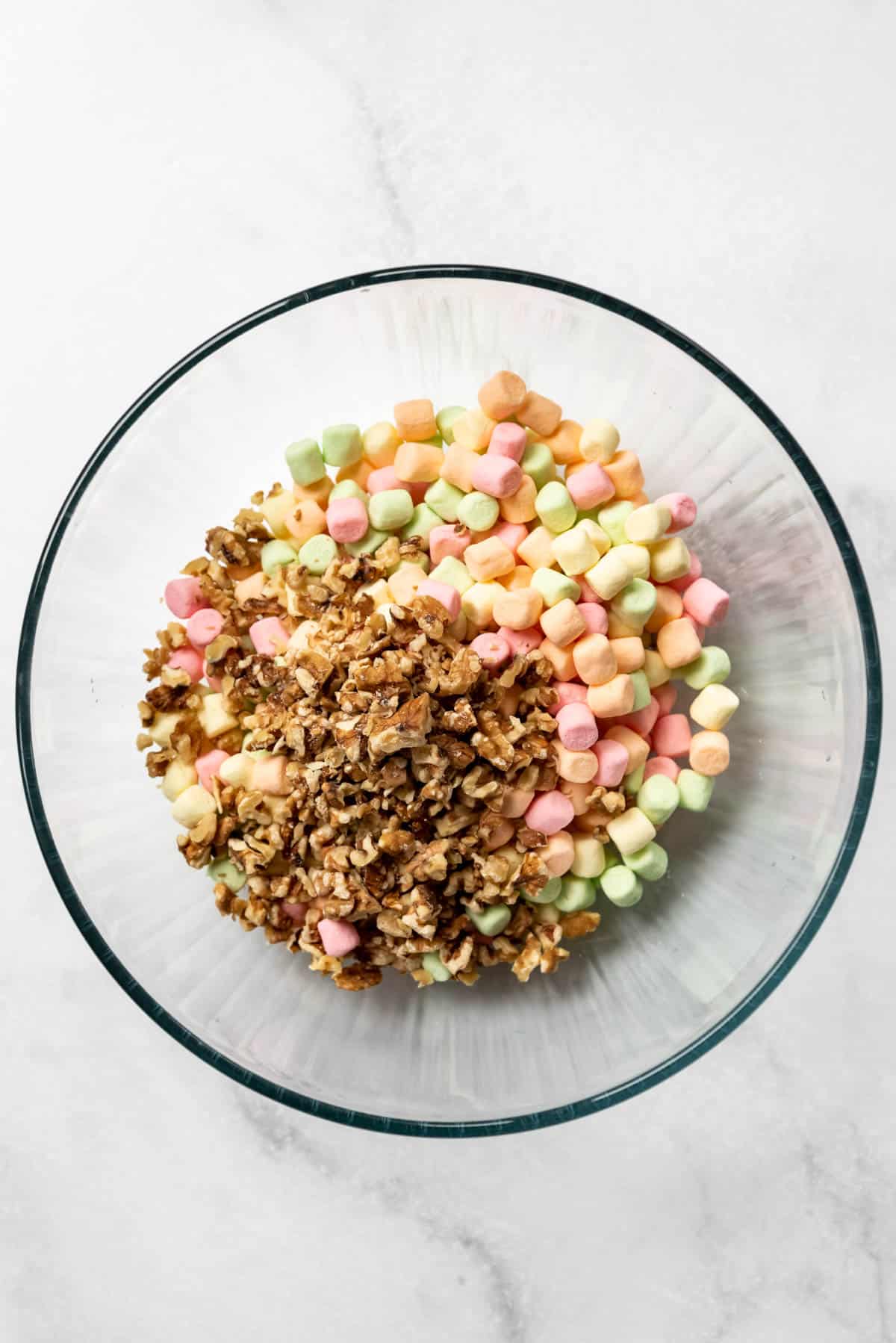 A glass bowl with multi-colored marshmallows and chopped walnuts.