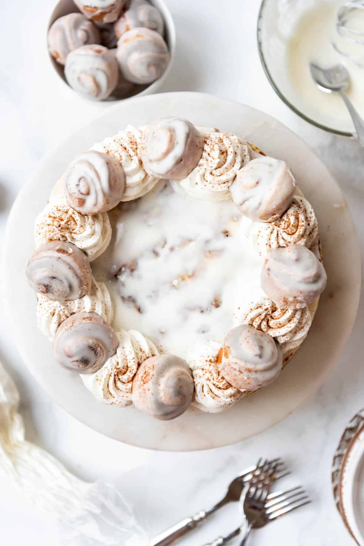 A cinnamon roll cheesecake decorated with swirls of whipped cream and mini cinnamon rolls.