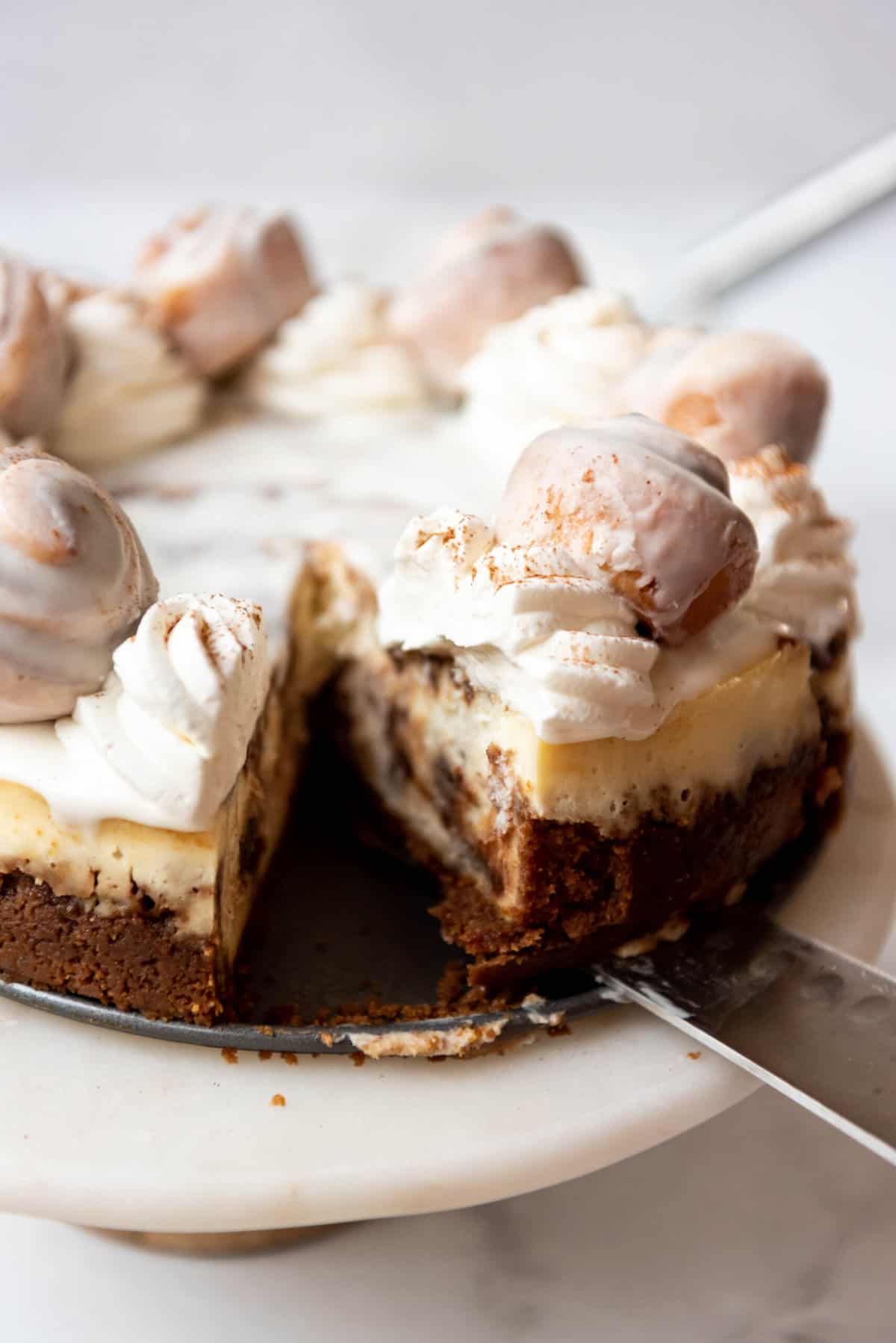 Removing a slice of cinnamon roll cheesecake from a cake plate.