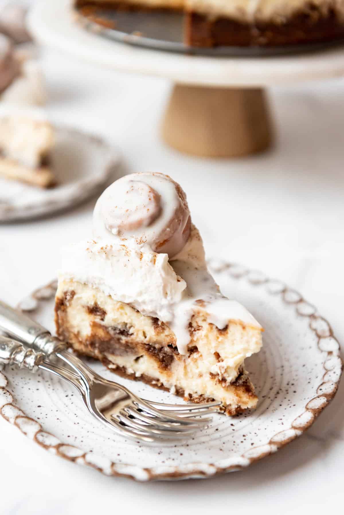 A slice of cinnamon roll cheesecake on a plate with two forks.