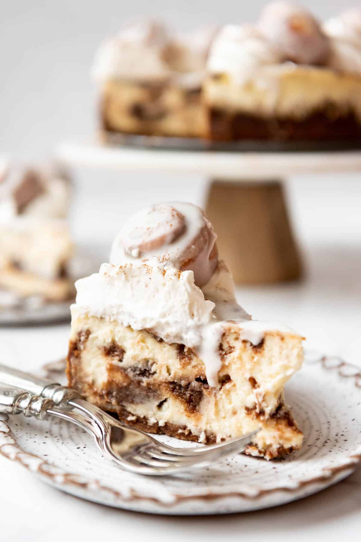 A slice of cinnamon swirl cheesecake in front of the rest of the cheesecake on a cake stand.