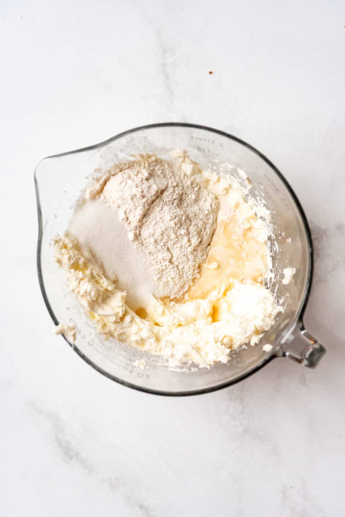 Adding flour, sugar, sour cream, heavy cream, and vanilla extract to cheesecake filling.