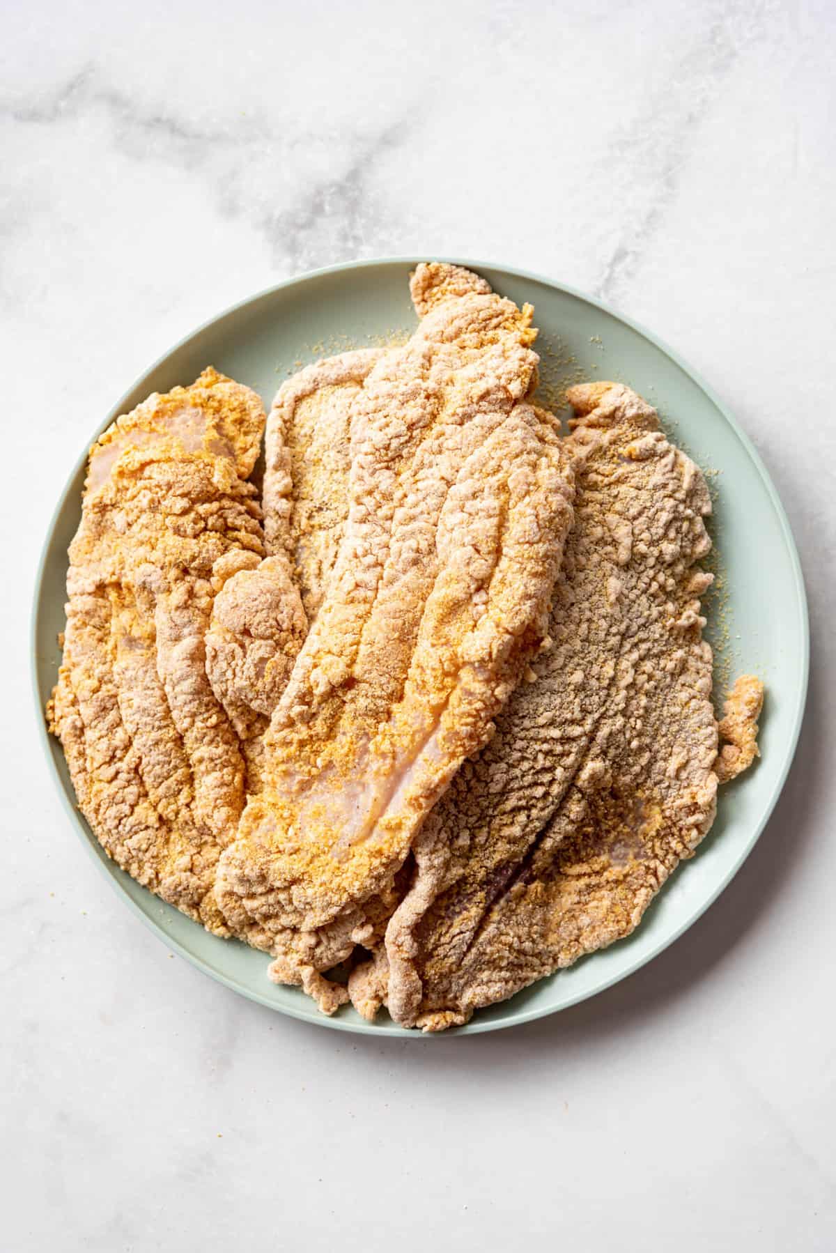 Catfish filets that have been coated in a spiced cornmeal breading on a plate.