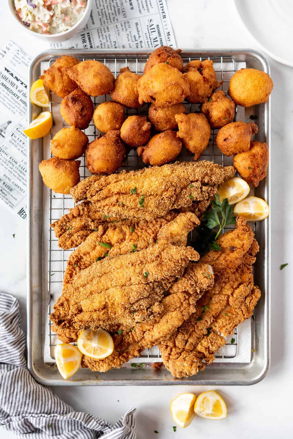 Pieces of fried catfish and fried hush puppies on a baking sheet.