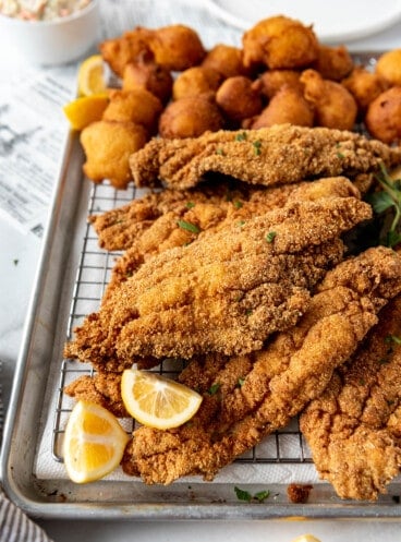 Fried catfish on a wire rack over a baking sheet with hush puppies.
