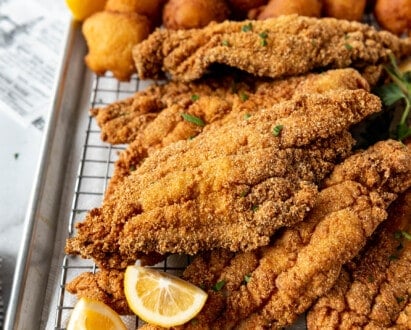 Fried catfish on a wire rack over a baking sheet with hush puppies.
