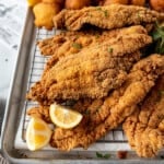 An image of fried catfish on a wire rack with lemon wedges.