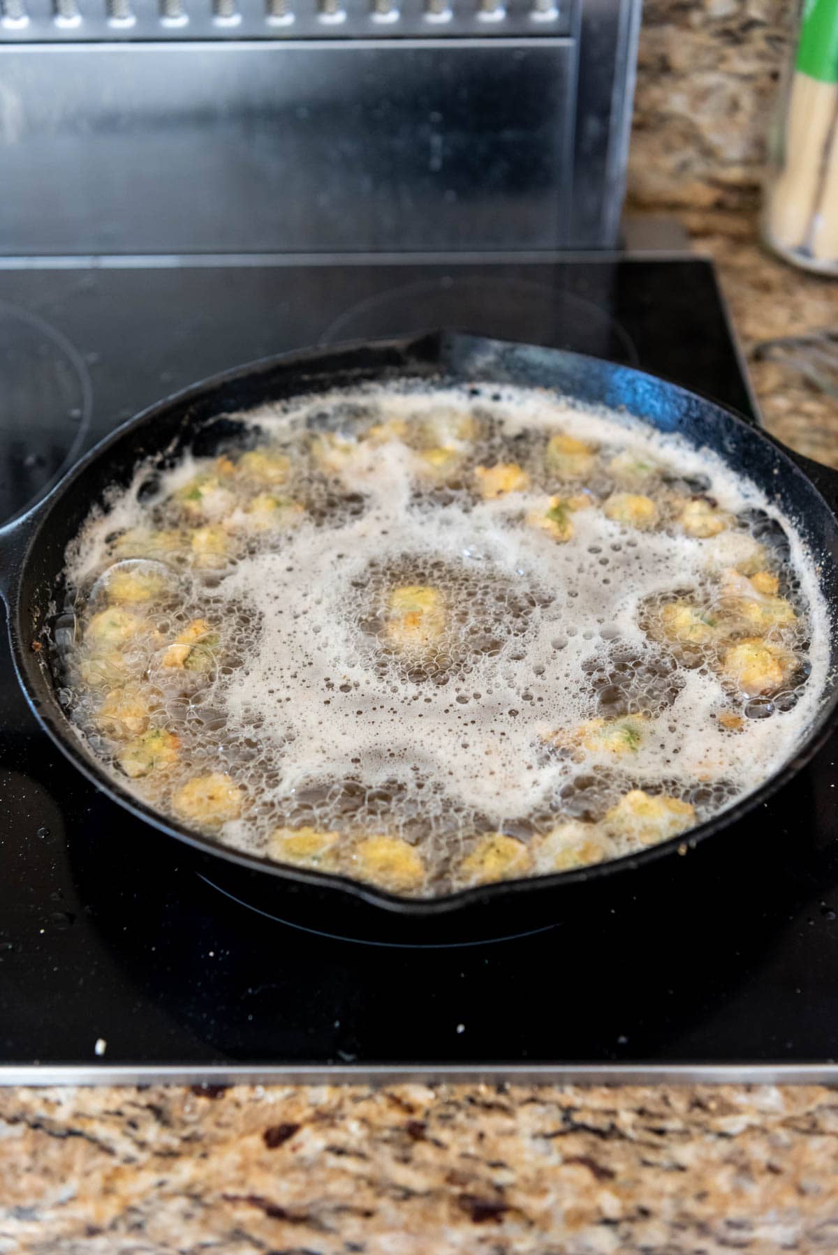 Frying okra in hot oil in a cast iron pan on the stove.