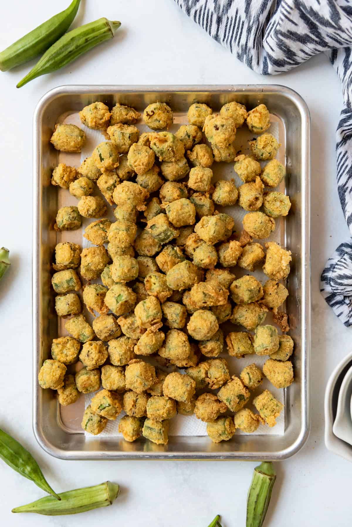 Fried okra on a baking sheet draining onto paper towels.