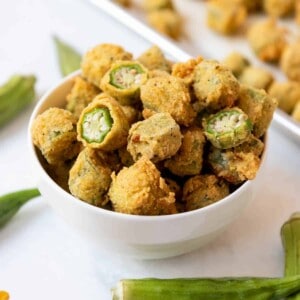 A bowl of fried okra with some fresh okra surrounding it.