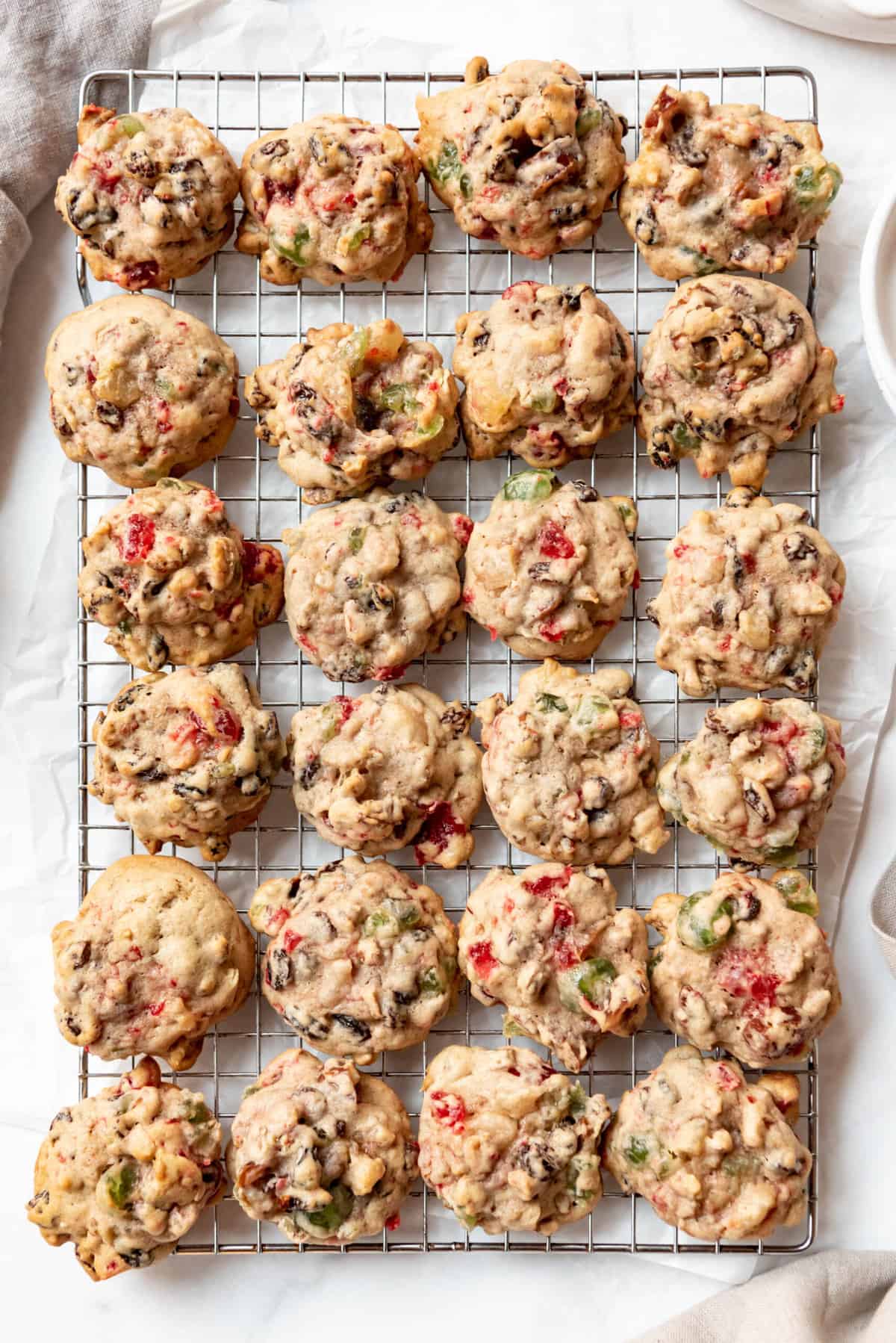 A batch of fruitcake cookies made with chopped candied cherries, pineapple, dates, and nuts on a wire cooling rack.