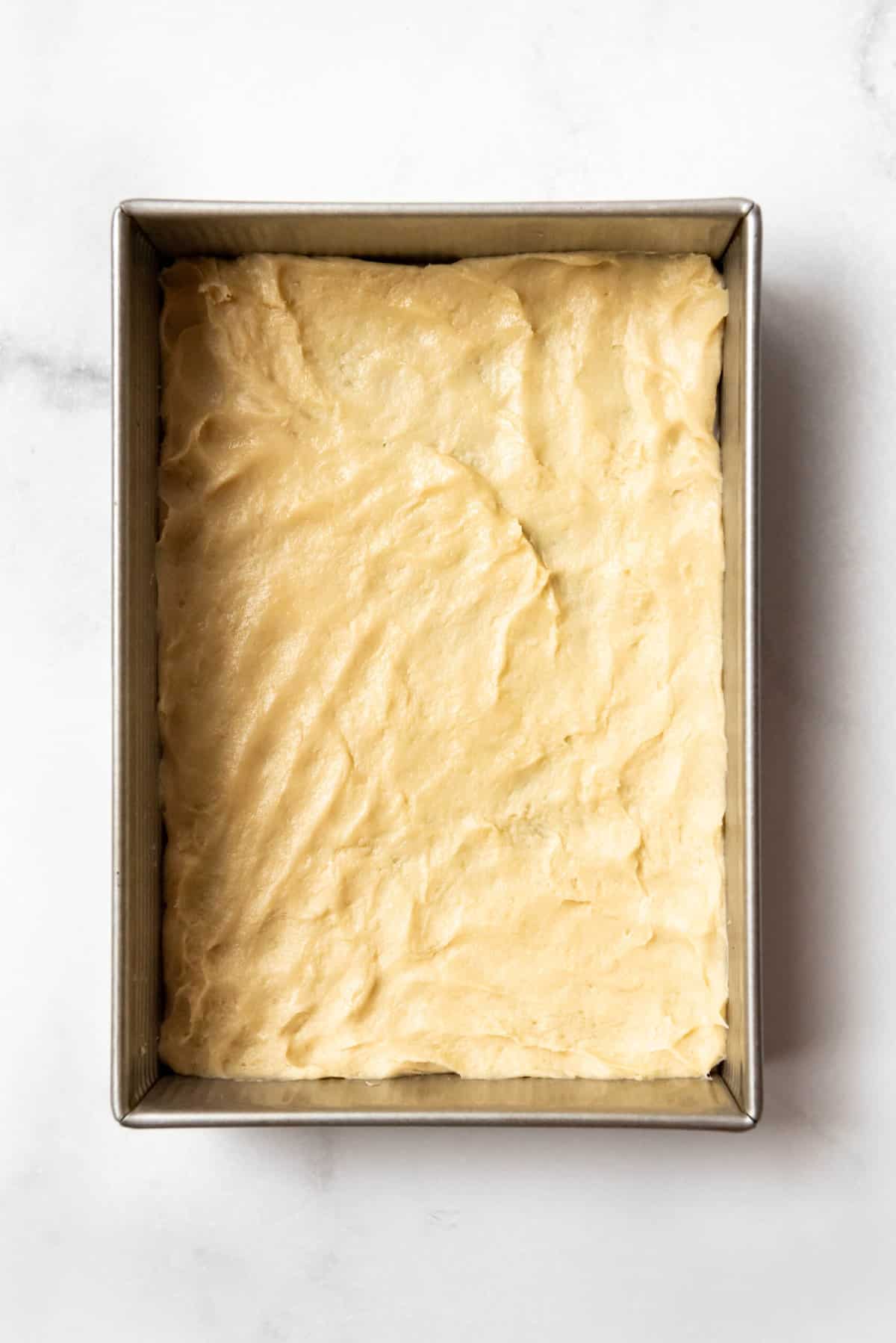 Top view of cake dough pressed into an even layer on the bottom of a pan.