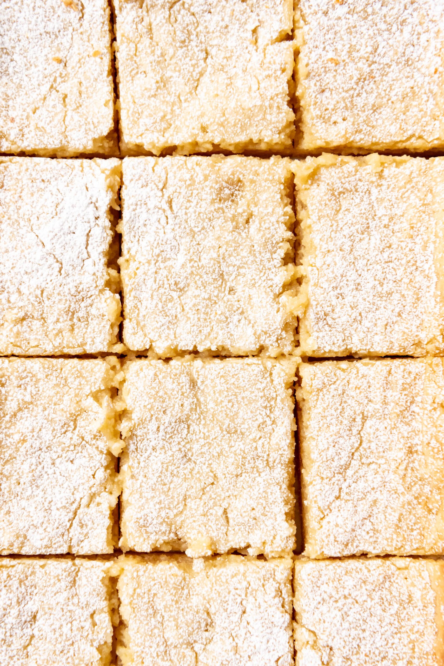 A close images of squares of gooey butter cake with powdered sugar dusted on top.
