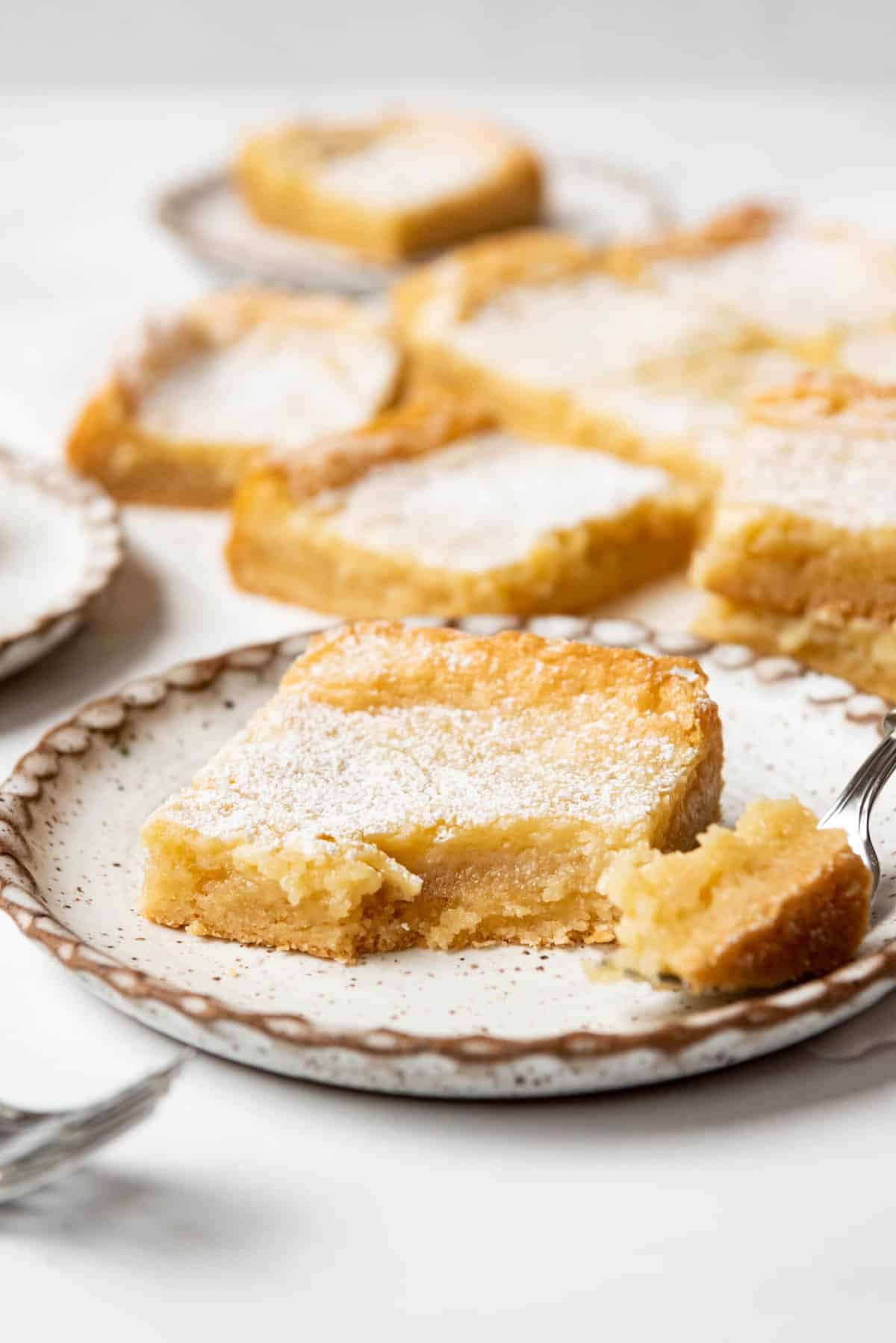 A slice of St. Louis gooey butter cake on a plate with a bite taken out of it.