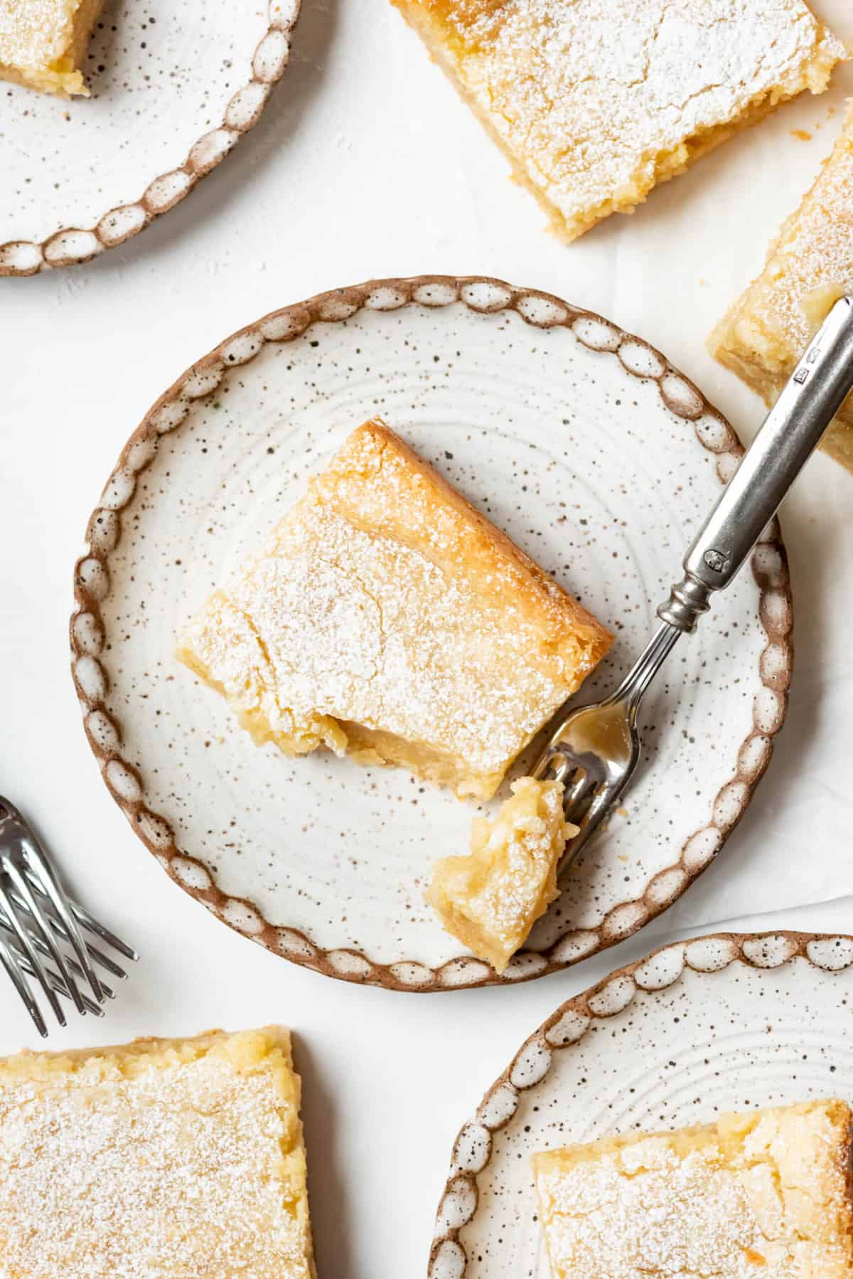 An overhead angle of a piece of gooey butter cake with one bite taken out of it on a plate.