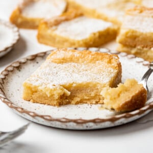 A piece of St. Louis gooey butter cake on a plate with a bite taken out of it.