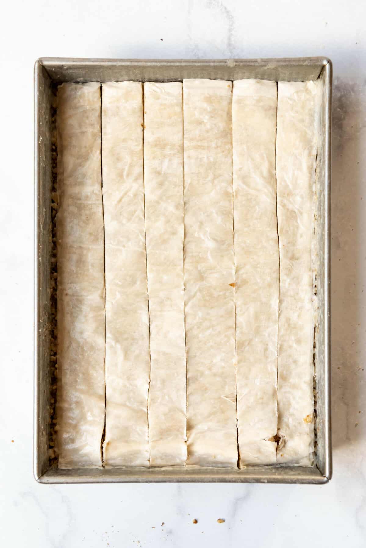 Cutting vertical lines through layers of phyllo dough and nuts.