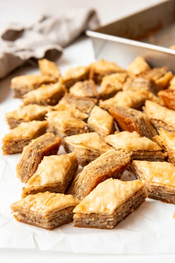 Slices of baklava with walnuts and honey scattered haphazardly next to a metal baking dish.