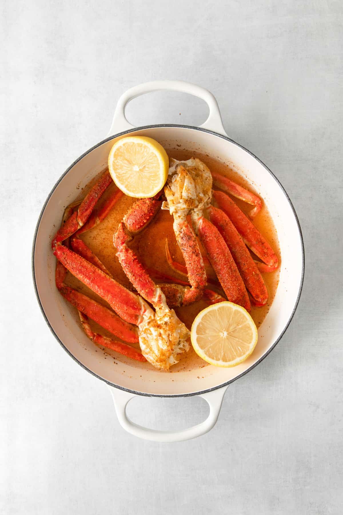 Crab legs and lemon halves in a large white dutch oven.