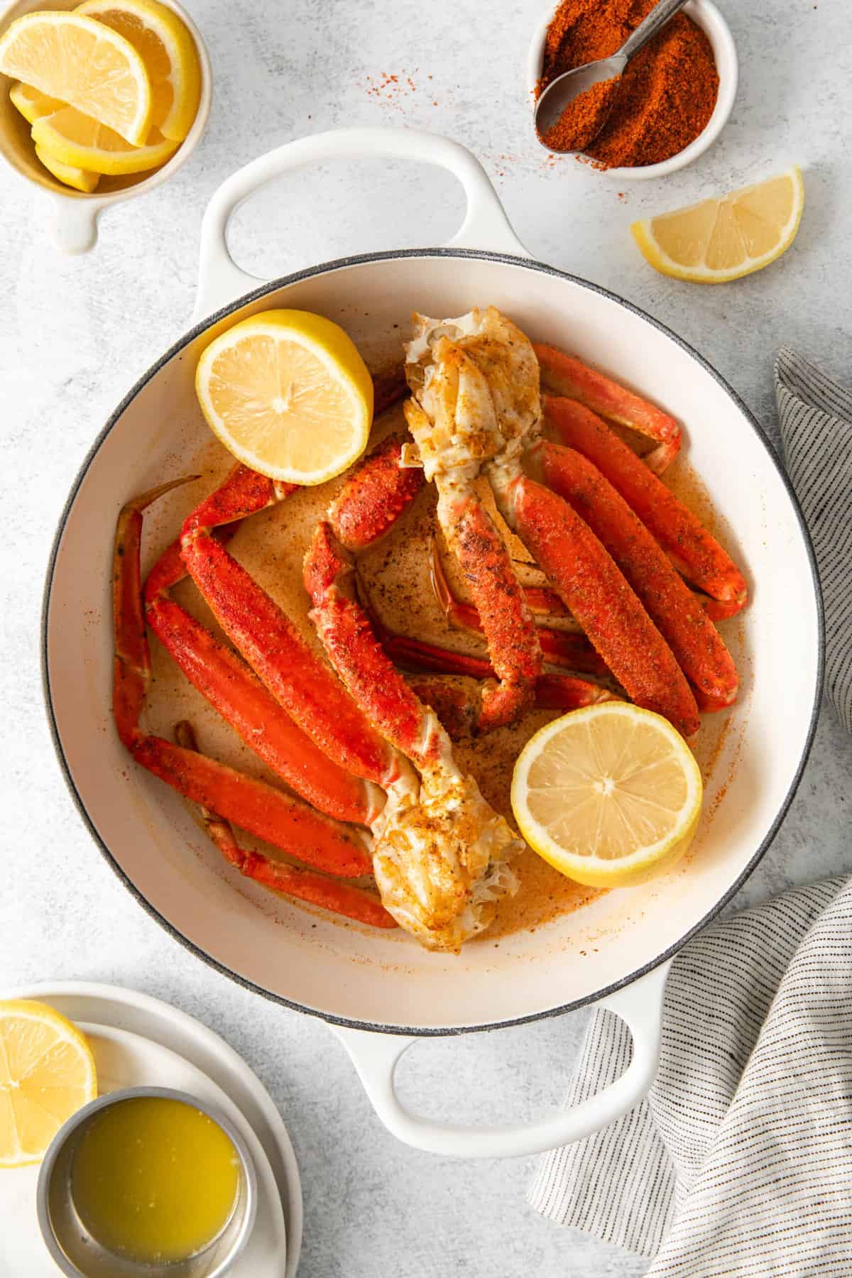 Snow crab legs in a white dutch oven with lemons and seafood seasoning nearby.