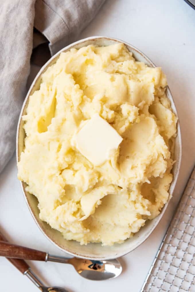 Top view of mashed potatoes in a serving dish with a small block of butter on top.