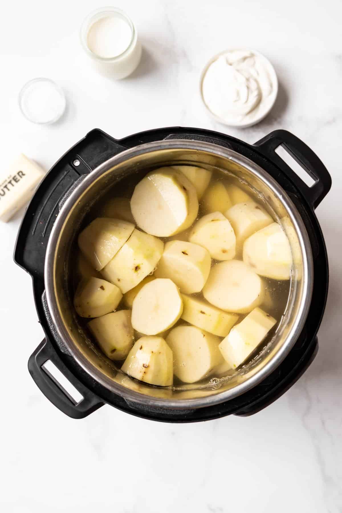 Top view of peeled potato halves in an instant pot with seasonings in small bowls next to it. 