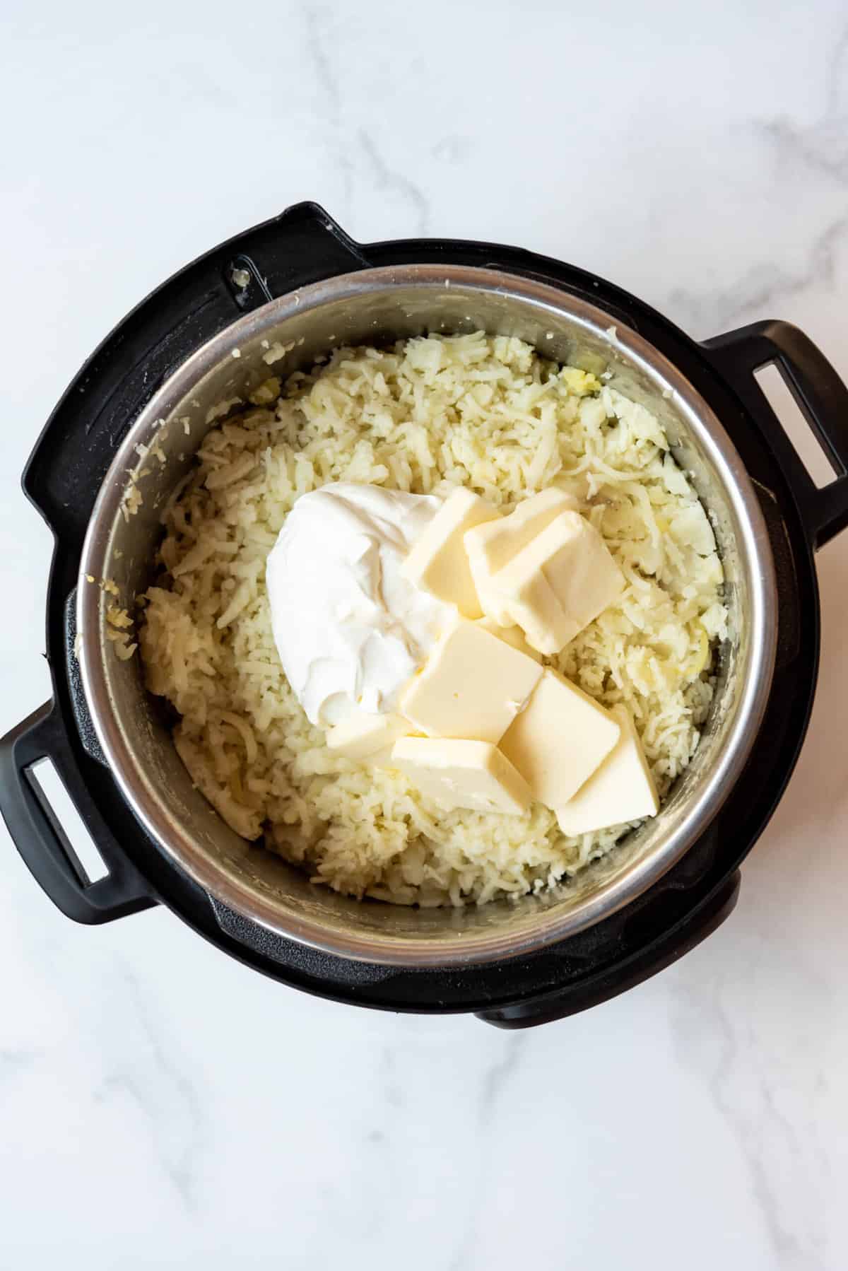Top view of mashed potatoes in an instant pot with cream cheese, butter and milk on top. 