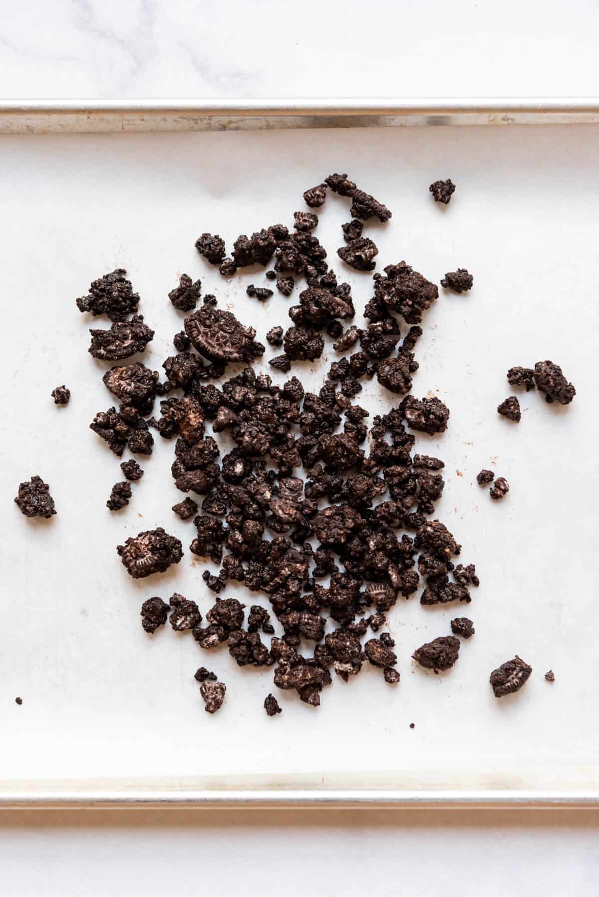 Crushed Oreo pieces tossed with butter and cocoa powder on a baking sheet lined with parchment paper.
