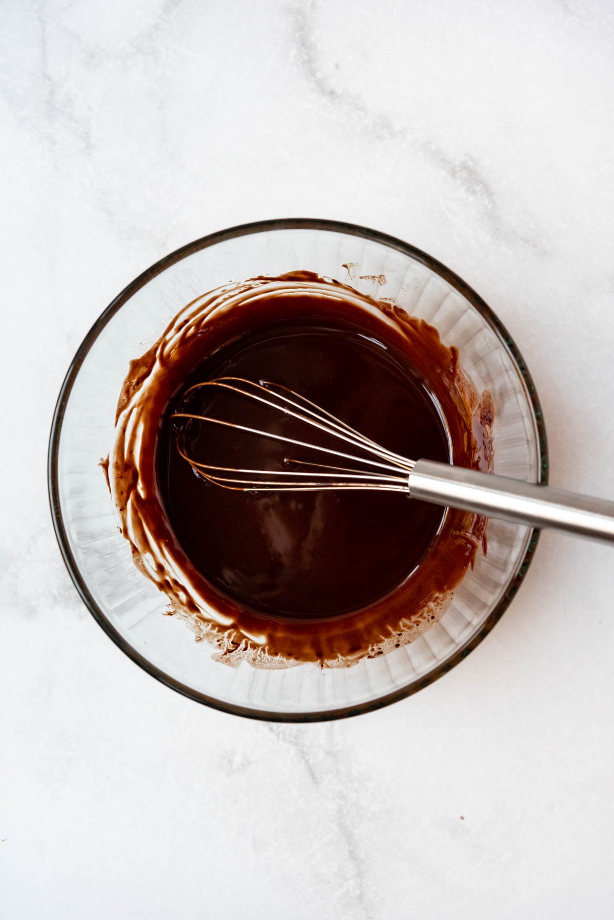 Whisking melted butter and chocolate in a glass bowl.