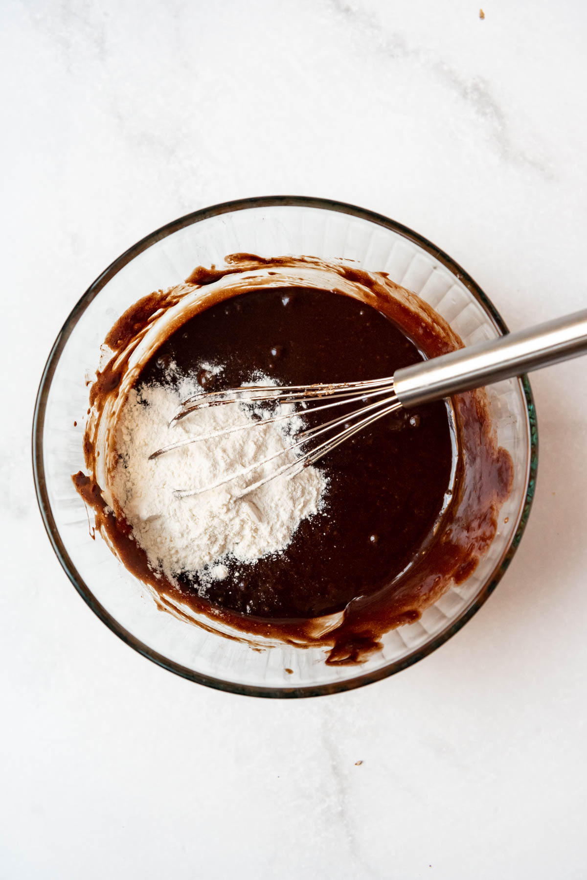 Whisking flour into chocolate batter in a glass bowl.