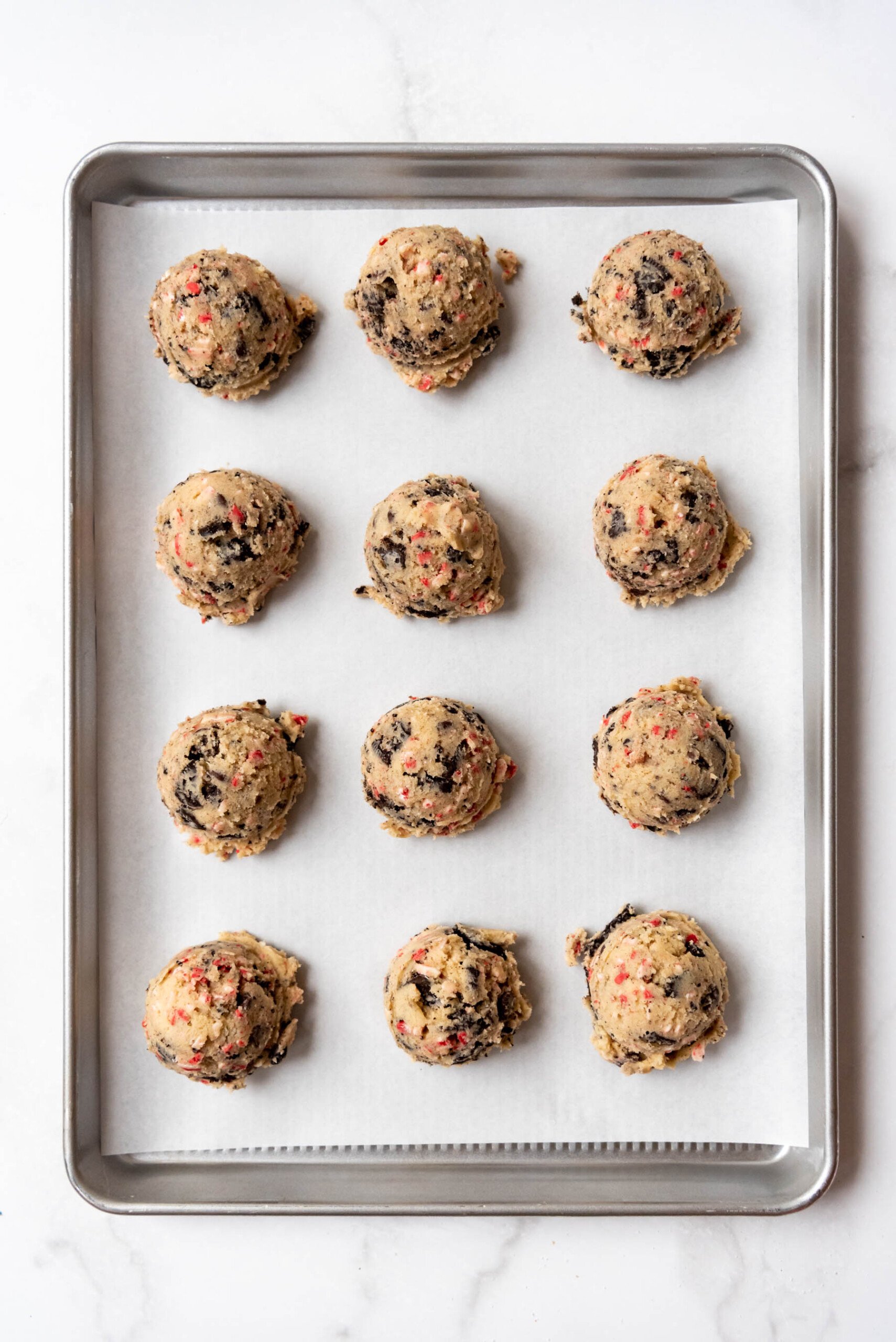 Balls of peppermint Oreo cookie dough on a baking sheet lined with parchment paper.