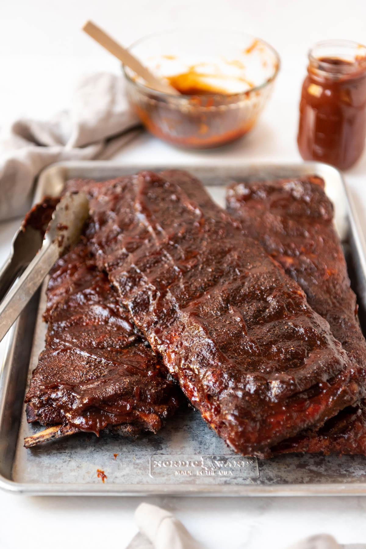 Cooked St. Louis-style ribs on a baking sheet in front of bowls of Kansas City BBQ sauce.