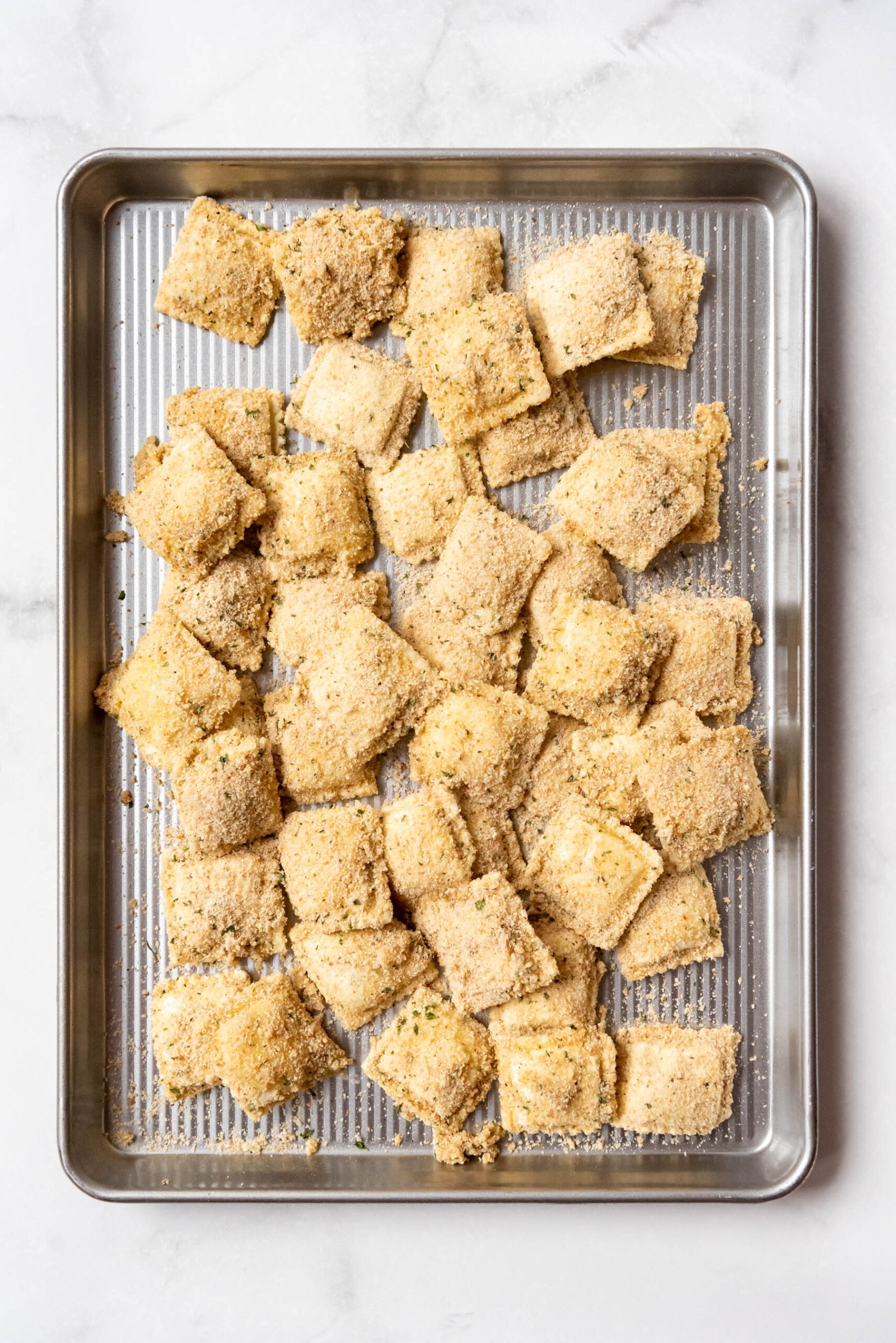 Breaded frozen cheese ravioli on a baking sheet ready to be cooked.