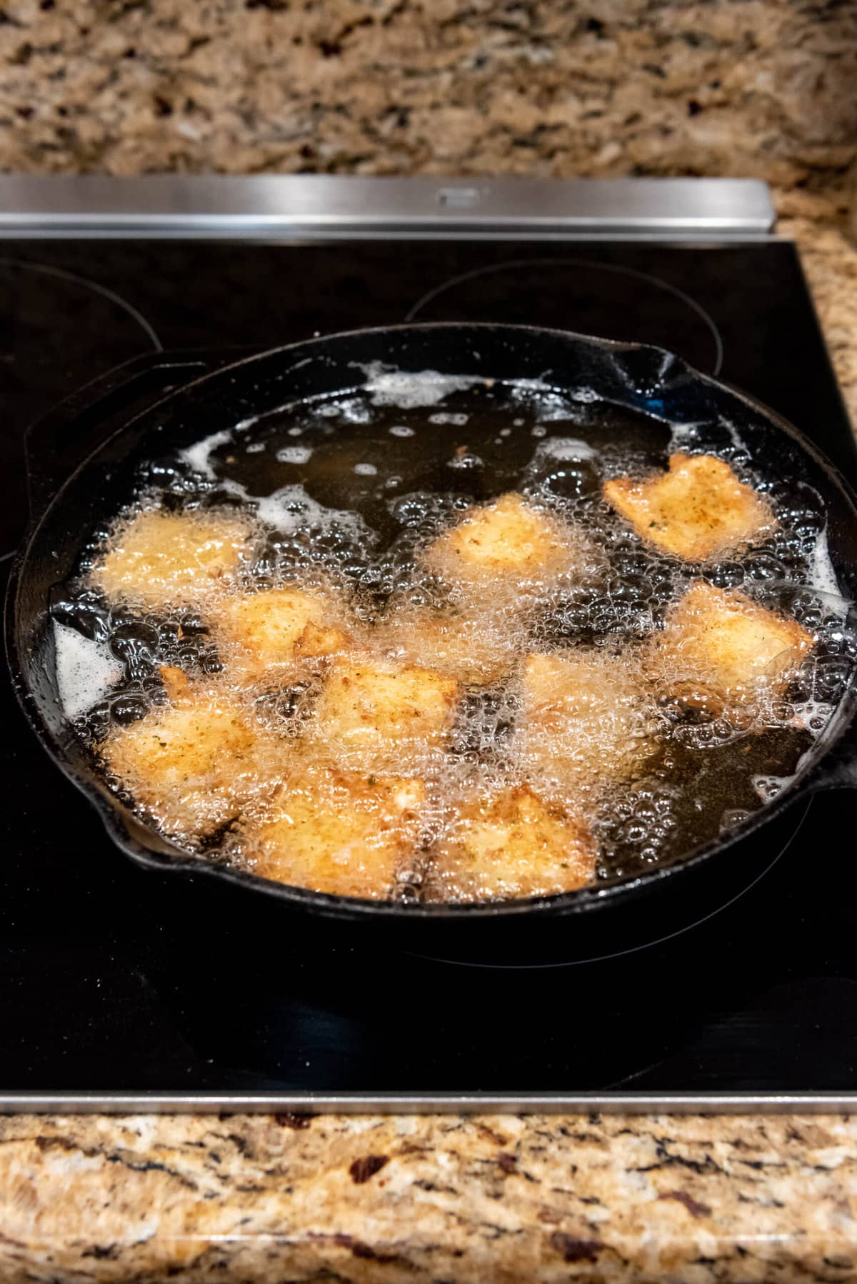 Ravioli being fried in a large skillet filled with hot oil