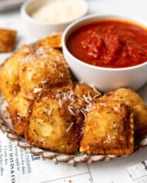 Toasted ravioli on a plate with a bowl of marinara dipping sauce.