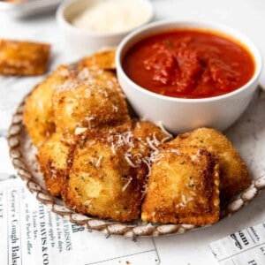 Toasted ravioli on a plate with a bowl of marinara dipping sauce.