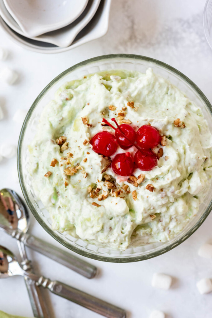 An overhead image of a bowl of watergate salad with chopped pecans and maraschino cherries on top.